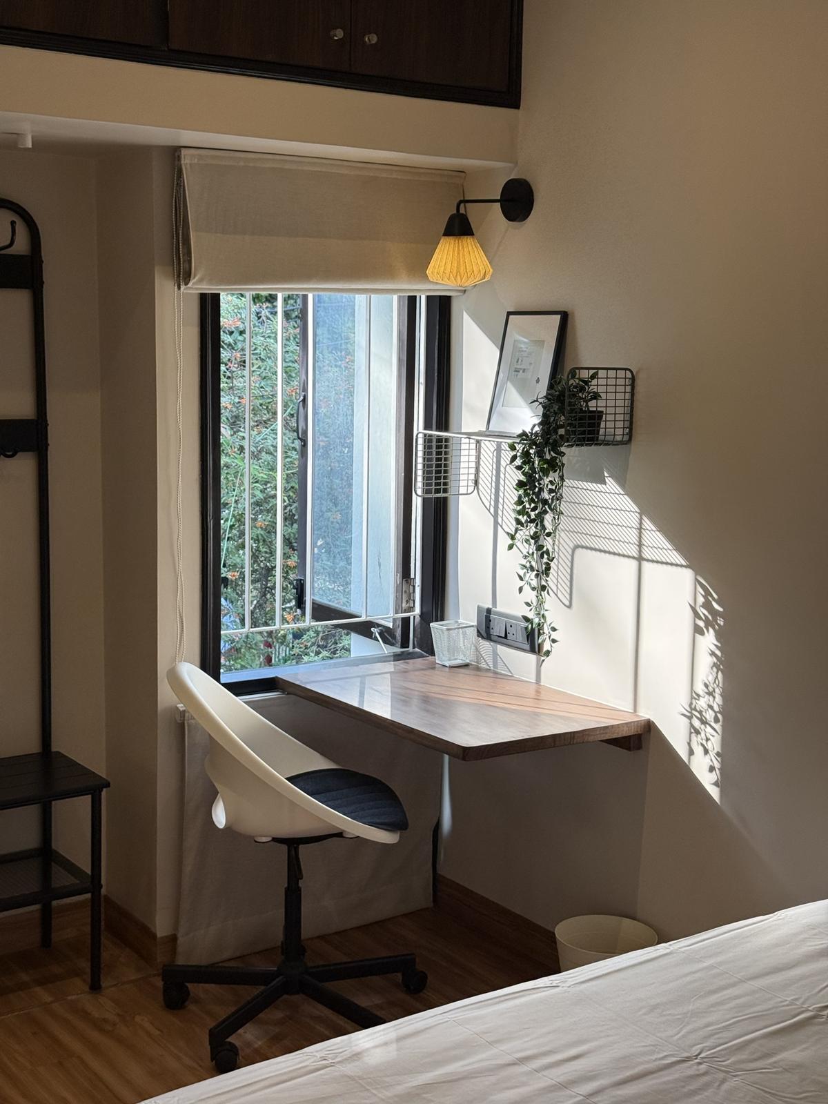 A wooden desk at an open window, trees outside and leaf shadows on the wall
